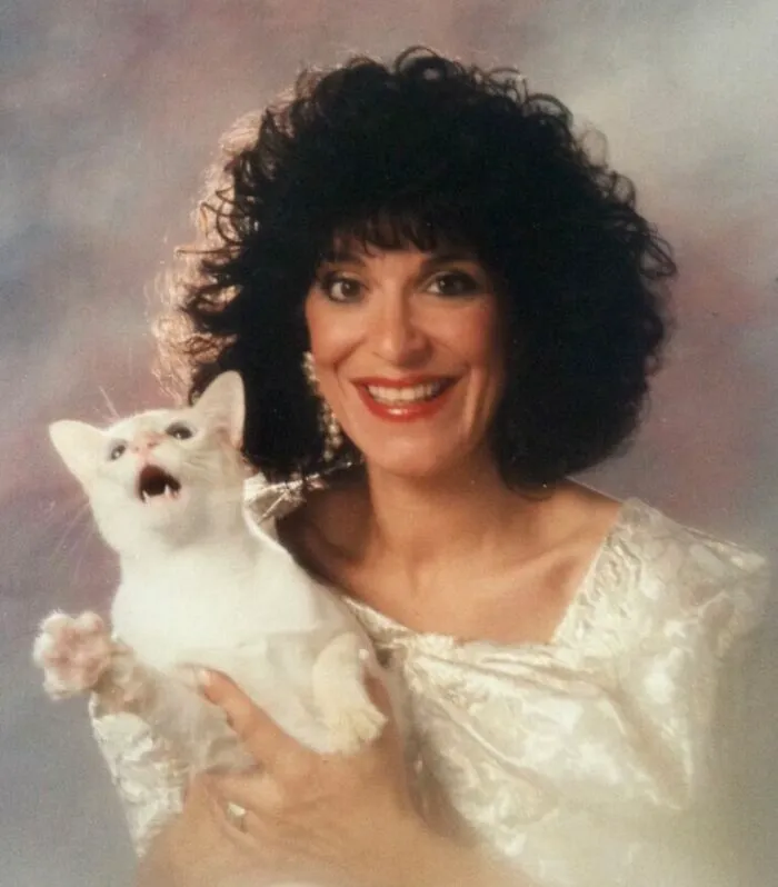 An awkward studio family portrait with a woman and a startled white cat showing hilarious facial expressions.