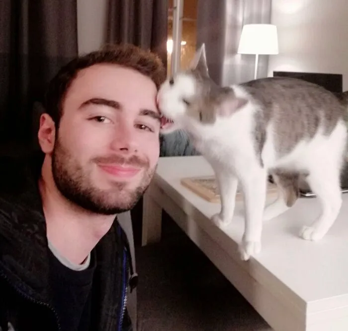 A man smiling as his cat bites his forehead during hilarious family photos with cats.
