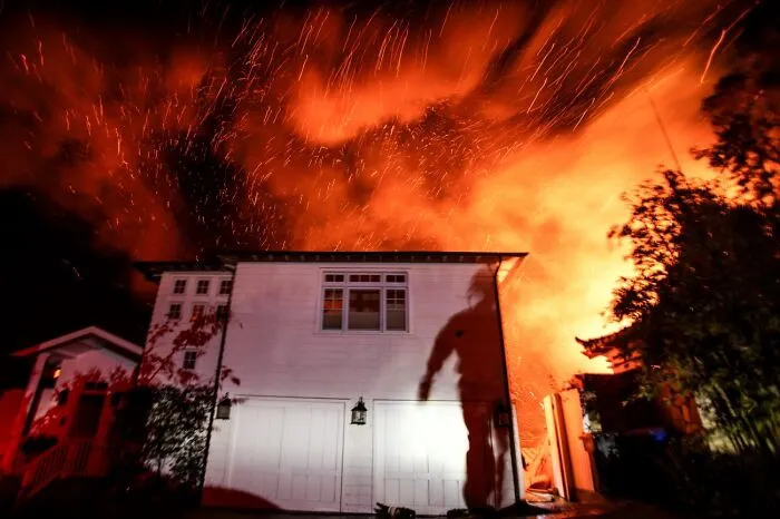 Housefire at night with bright flames and shadow of person on wall