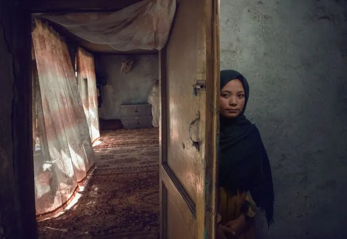 Girl peeking from behind door in rustic home, best pics Siena International Photo Awards 2026