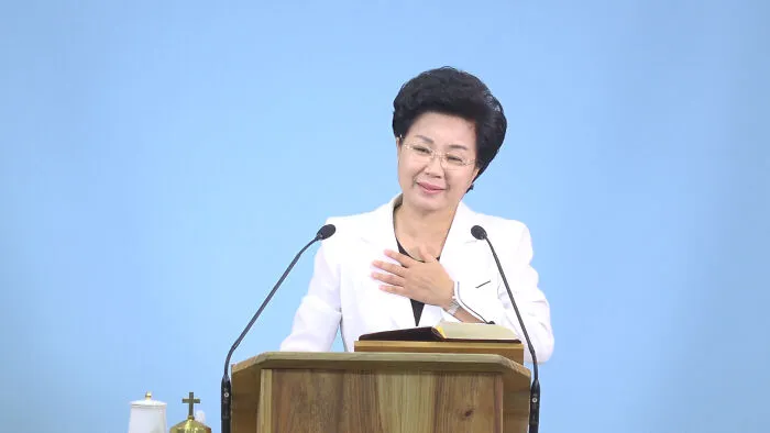 A woman speaking at a podium in a setting linked to lesser-known cults.
