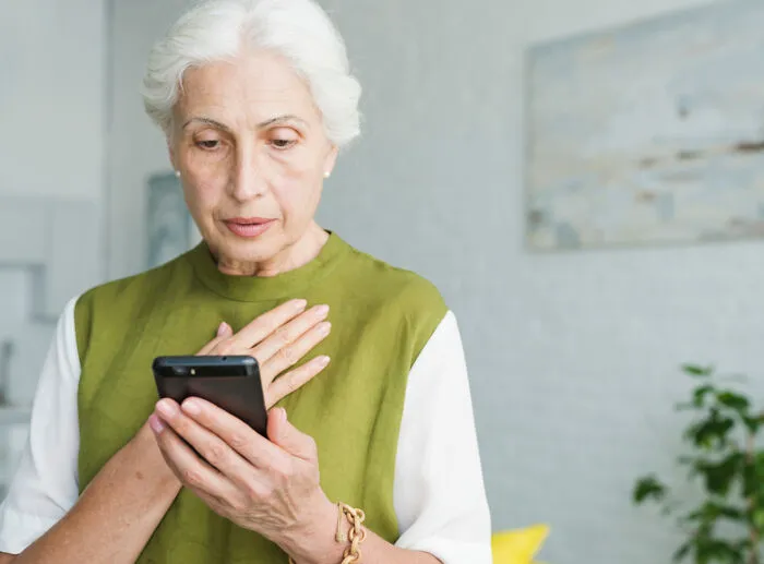 An anxious elderly woman holding a smartphone, shocked by crazy mil stories.