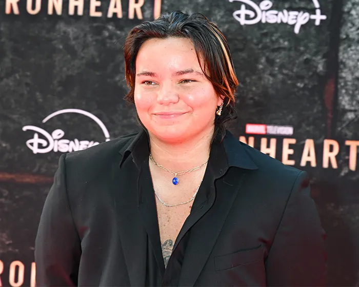 Trans actor wearing a black suit posing at the Ironheart red carpet event in Hollywood