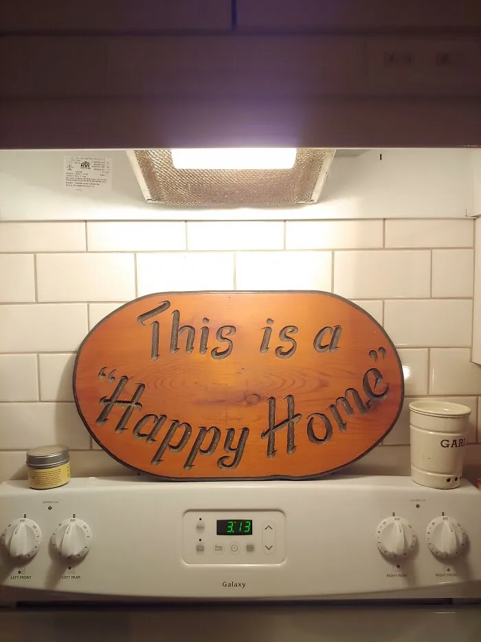 A wooden home sign above a stove misused quotation marks around the words Happy Home.