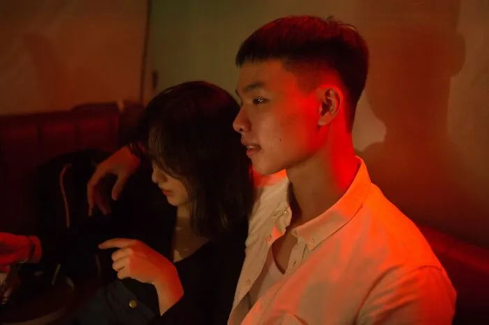 A young couple sitting closely together under red ambient lighting while sharing secrets