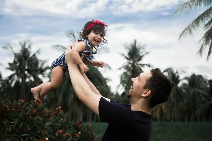 A happy father lifting his baby girl high in the air outdoors with secrets shared in the family