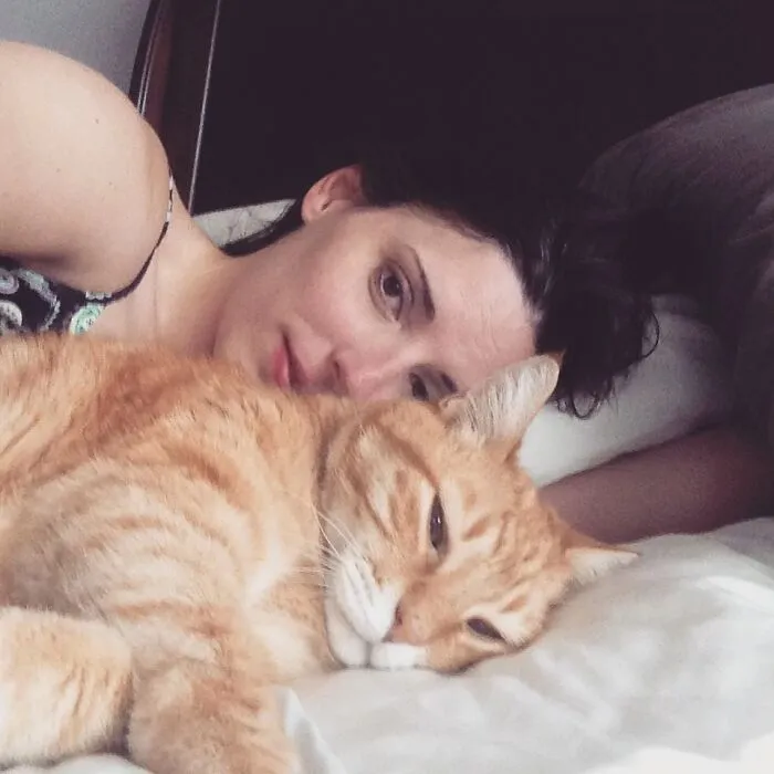 A woman and her orange cat lying down together, sharing life stories lived alongside their pets.