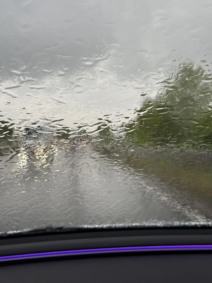 Raindrops covering a car windshield, presenting an absurd moment during rainy weather.