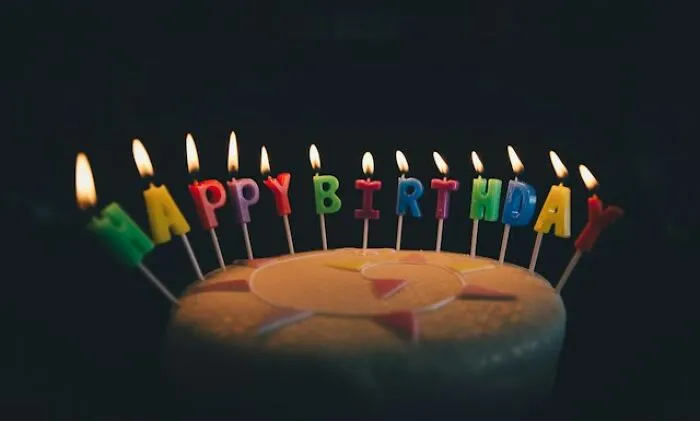 A birthday cake with lit colorful letter candles spelling out Happy Birthday, sharing ideas for celebrations