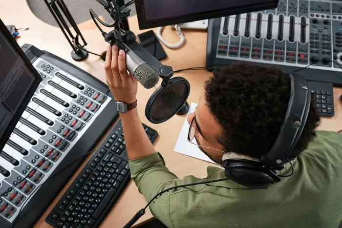 A radio host adjusting a microphone in a sound studio, working as an industry insider.