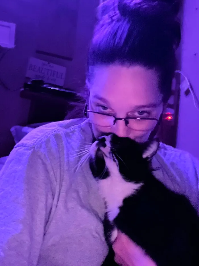 A woman with glasses cuddling her black and white tuxedo cat, sharing life stories with pets