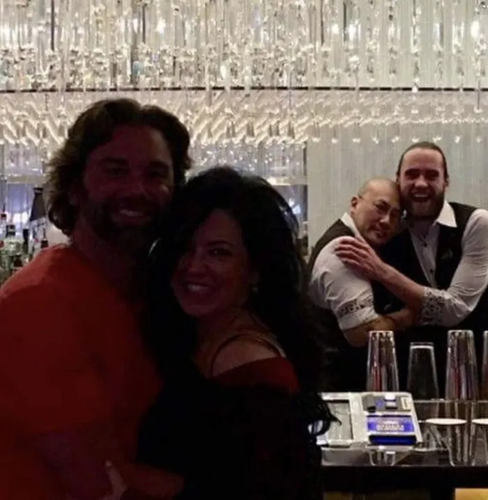 Funny background hijackers with two bartenders hugging in the background behind a smiling couple.