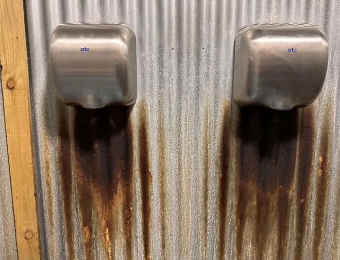 two hand dryers causing rust stains on corrugated metal wall