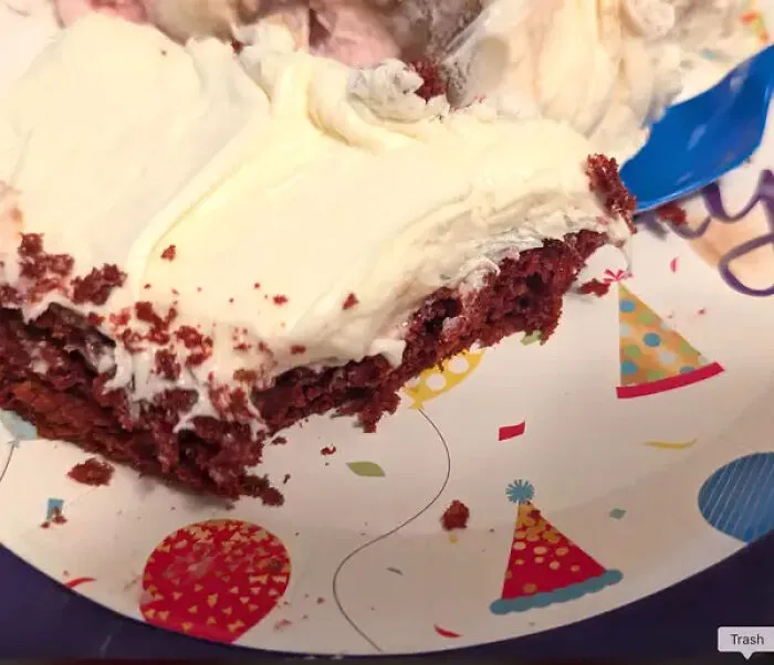 Piece of red velvet cake on a party plate with a blue plastic fork