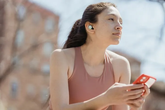 Young woman with earbuds holding phone showing basic life skills for personal care