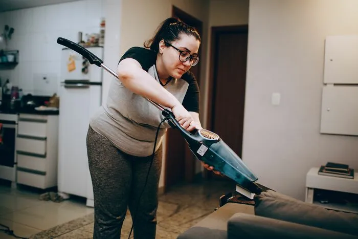 Woman vacuuming couch as part of basic cleaning life skills
