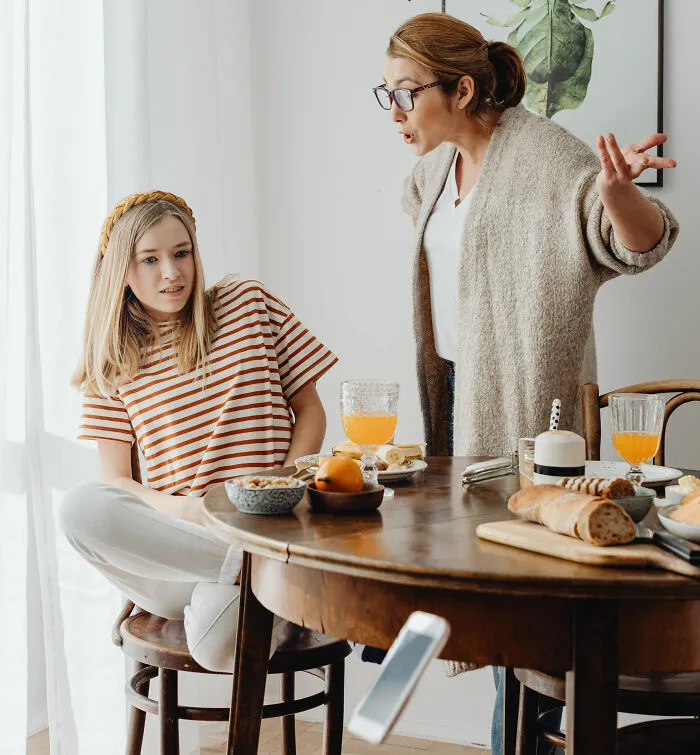 Mother angrily talking to daughter at breakfast table on basic life skills