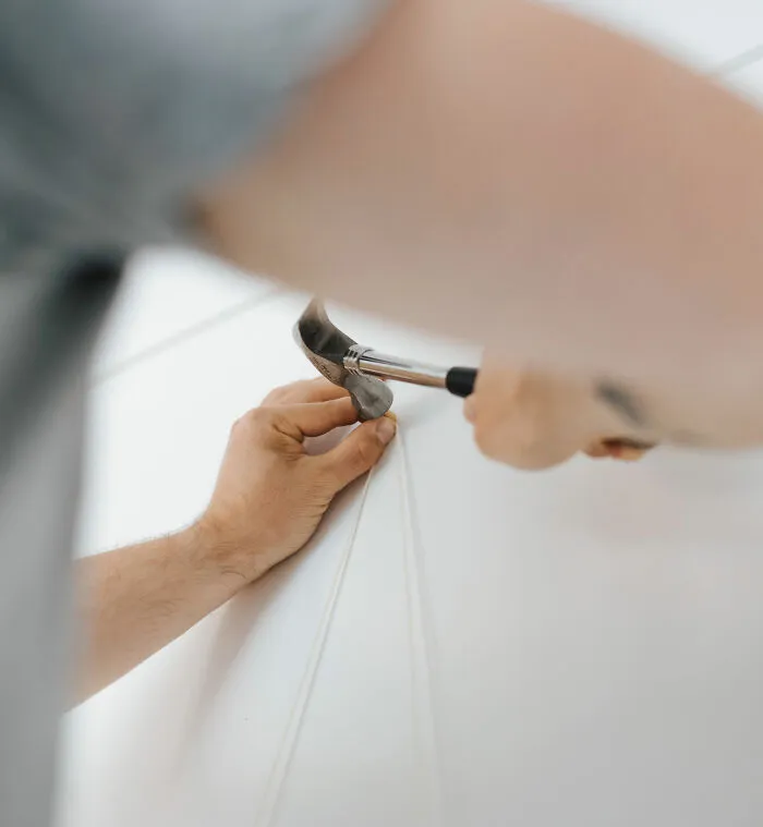 Person using hammer to remove a nail from wall demonstrating basic life skills