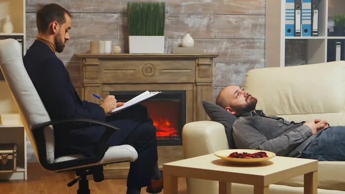 A man lying on a couch talking to his therapist in a quiet room, feeling sick and seeking help.