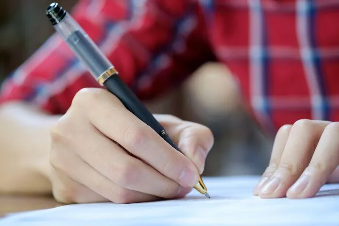 Close up of a hand writing on paper with a pen, crafting intelligent insults.