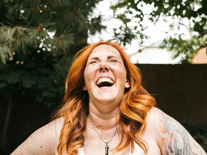 A redheaded woman laughing out loud outdoors, illustrating the humor of intelligent insults.