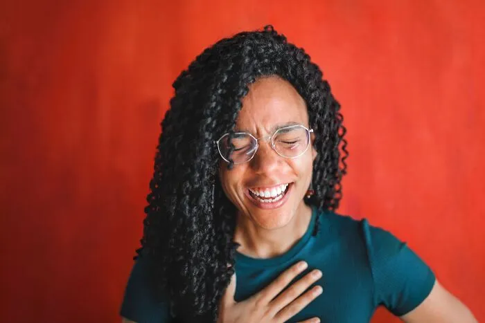 Person laughing heartily with eyes closed, amused by intelligent insults.