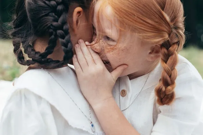 Young girl whispering to a friend, sharing witty and intelligent insults.