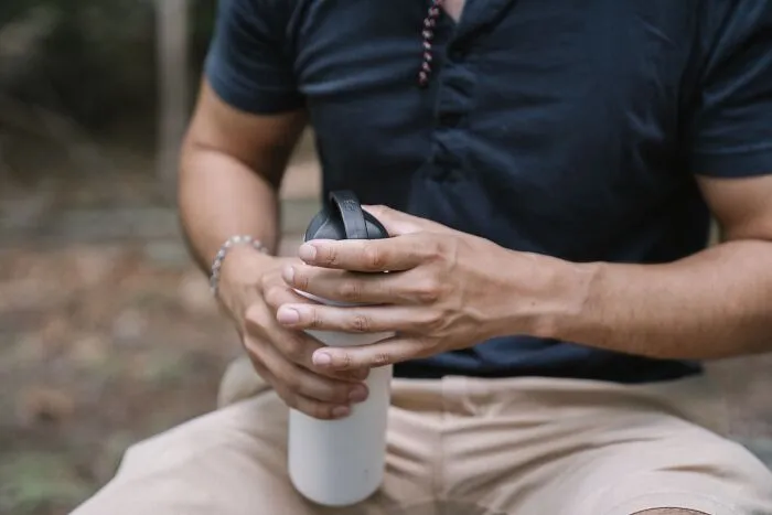 A man holding a reusable water bottle, reflecting on clever intelligent insults.
