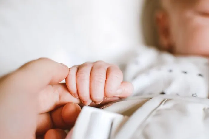 Close up of a baby holding an adult finger, symbolizing subtle intelligent insults.