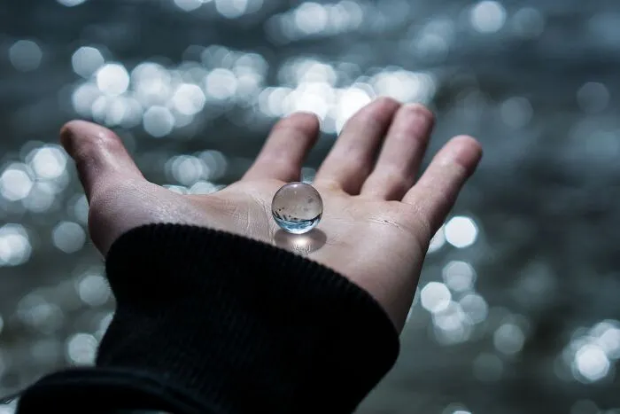A hand holding a clear glass marble over water, metaphorically representing intelligent insults.