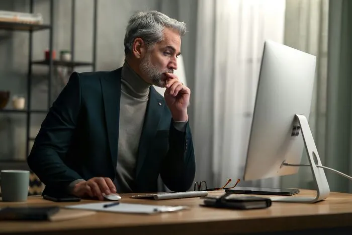 A thoughtful man sitting in front of a computer screen, processing intelligent insults.