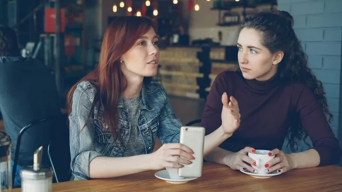 Two women having a serious conversation at a cafe, using intelligent insults.