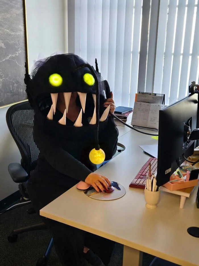 Woman sitting at a desk wearing a glowing anglerfish mask as a creative Halloween costume.