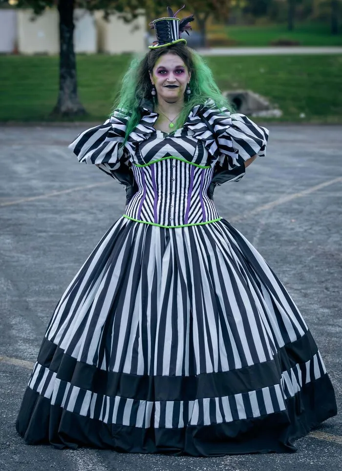 Woman in a detailed black and white striped gown and green hair presenting her Halloween costume.
