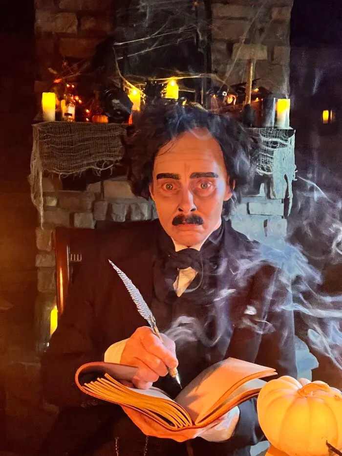 Person dressed up as Edgar Allan Poe in an impressive Halloween costume writing in a book.