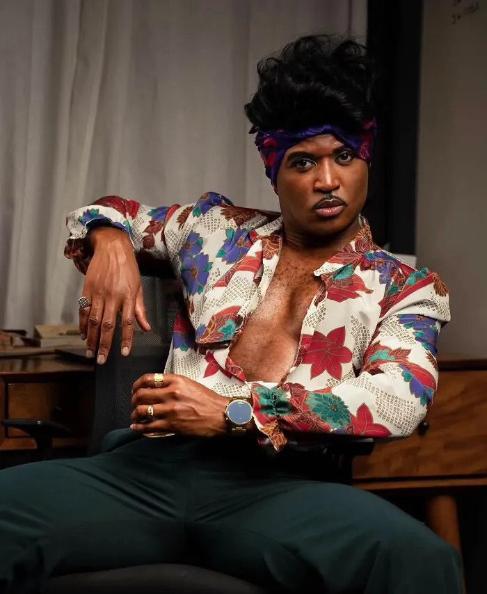 Person posing indoors dressed in a stylish, colorful vintage shirt as part of an impressive Halloween costume.
