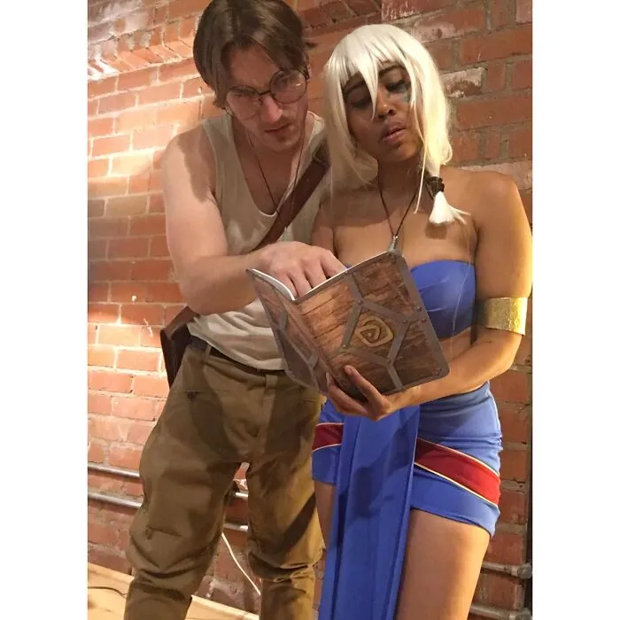 Couple dressed up in detailed Atlantis movie Halloween costumes reading a prop book together.