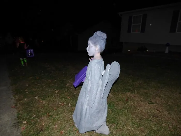 A young child dressed as a weeping statue in an impressive Halloween costume outdoors at night