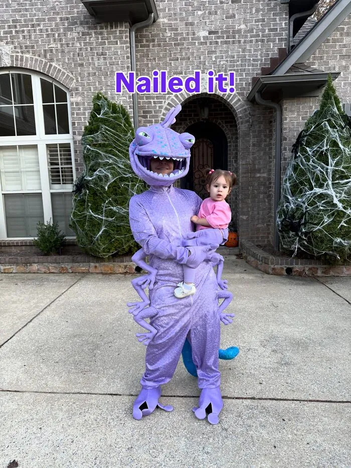 A person in a purple Randall monster suit holding a child in a fun Halloween costume