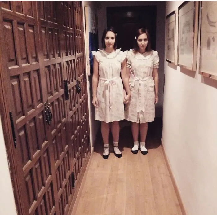 Two women dressed up in spooky creepy twin dresses as creative Halloween costumes in a hallway.