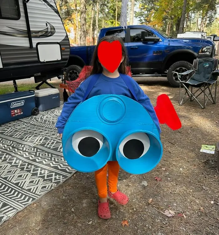 Child wearing a creative homemade view-master toy Halloween costumes while standing outdoors near a campsite.