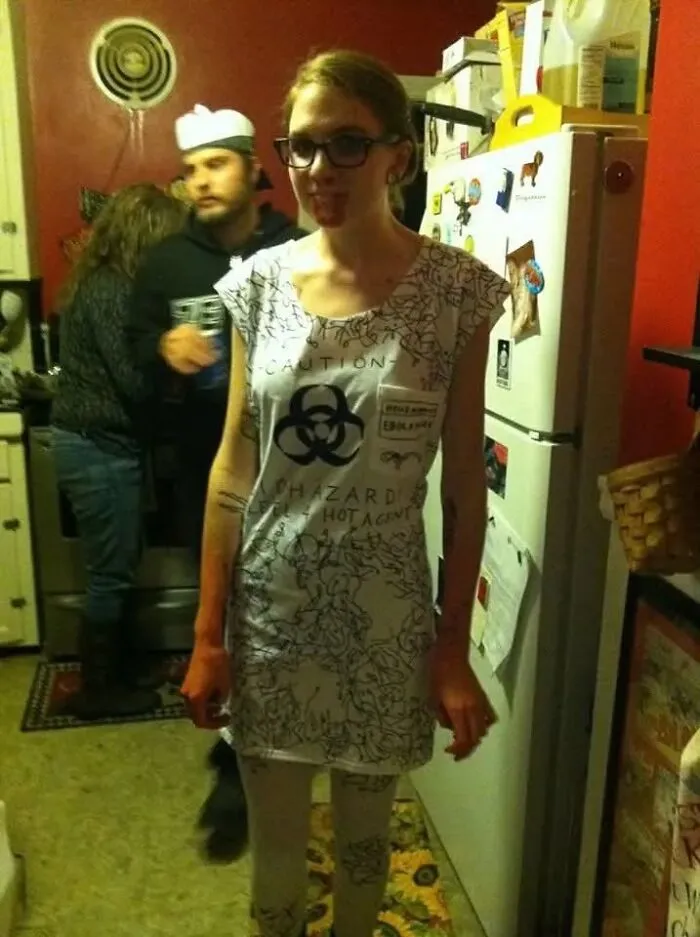 Woman posing in a white dress featuring a biohazard sign, wearing an creative Halloween costume.