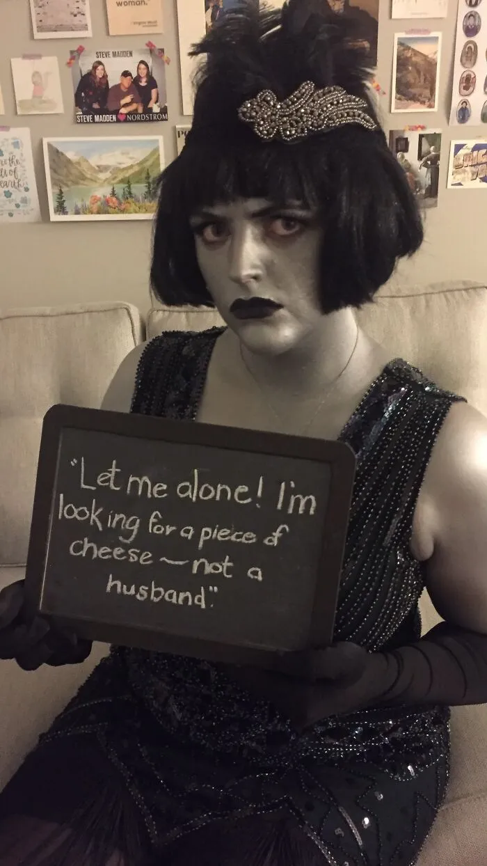 Woman in grayscale flapper Halloween costume holding a chalkboard sign looking for a piece of cheese