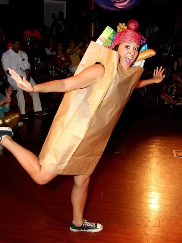 Woman posing dynamically in a creative paper grocery bag Halloween costume filled with baguettes and produce