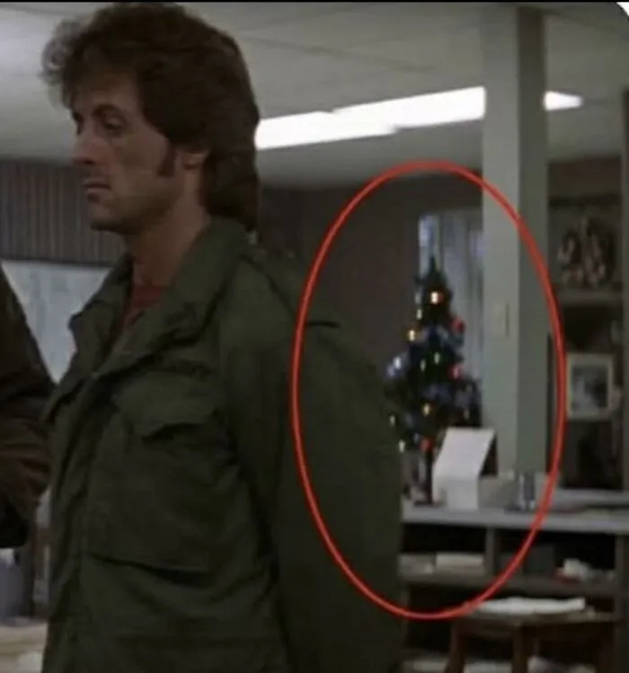 A man standing in a scene from First Blood with a Christmas tree circled in red, a nostalgic photo for 80s kids.