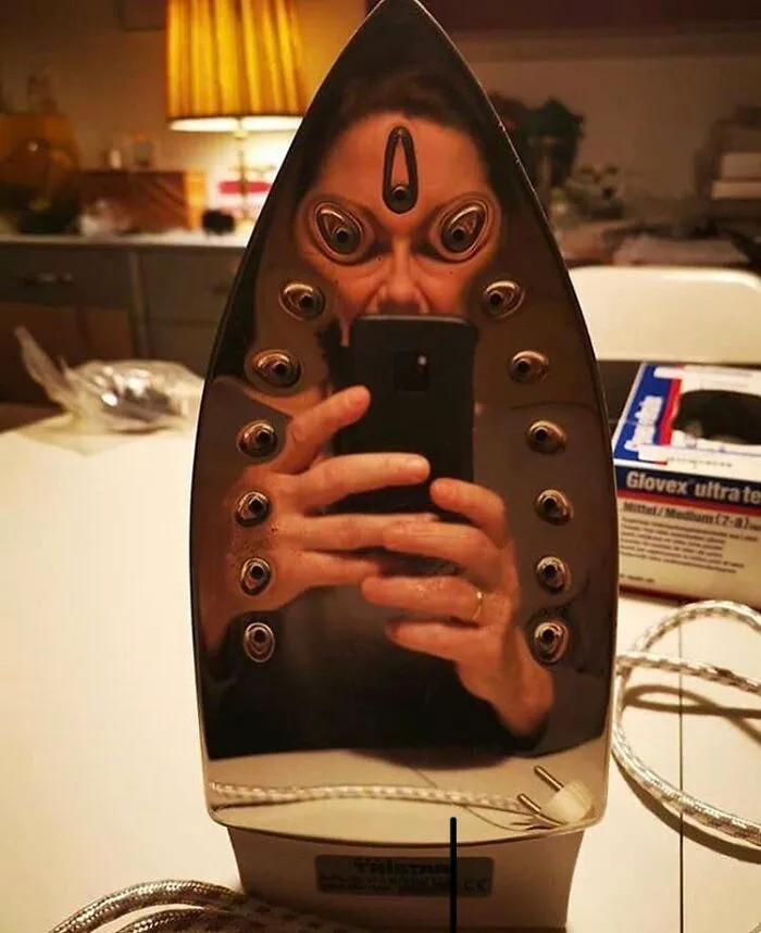 A perfectly confusing reflection of a person taking a photo in a clothes iron plate.