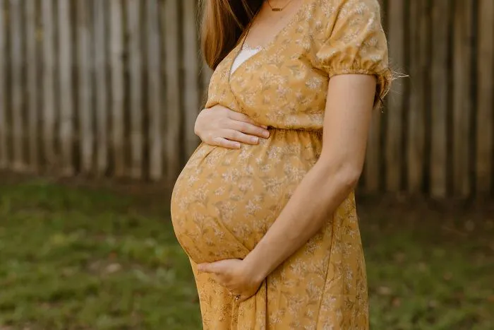 Pregnant woman in a yellow floral dress holding her belly, representing topics about narcissistic parents.