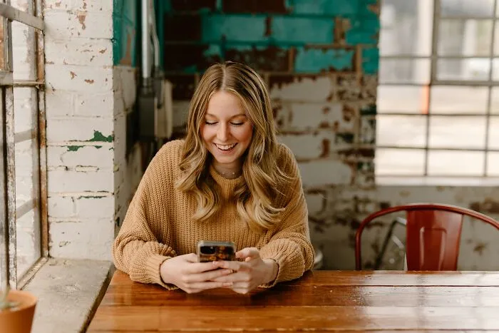 A smiling young woman sitting at a table looking at her smartphone, representing men wrong about women's bodies.