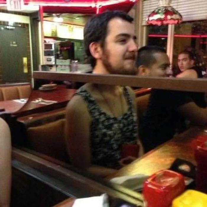 Optical illusion mirror reflection blending a bearded man face with another person body.