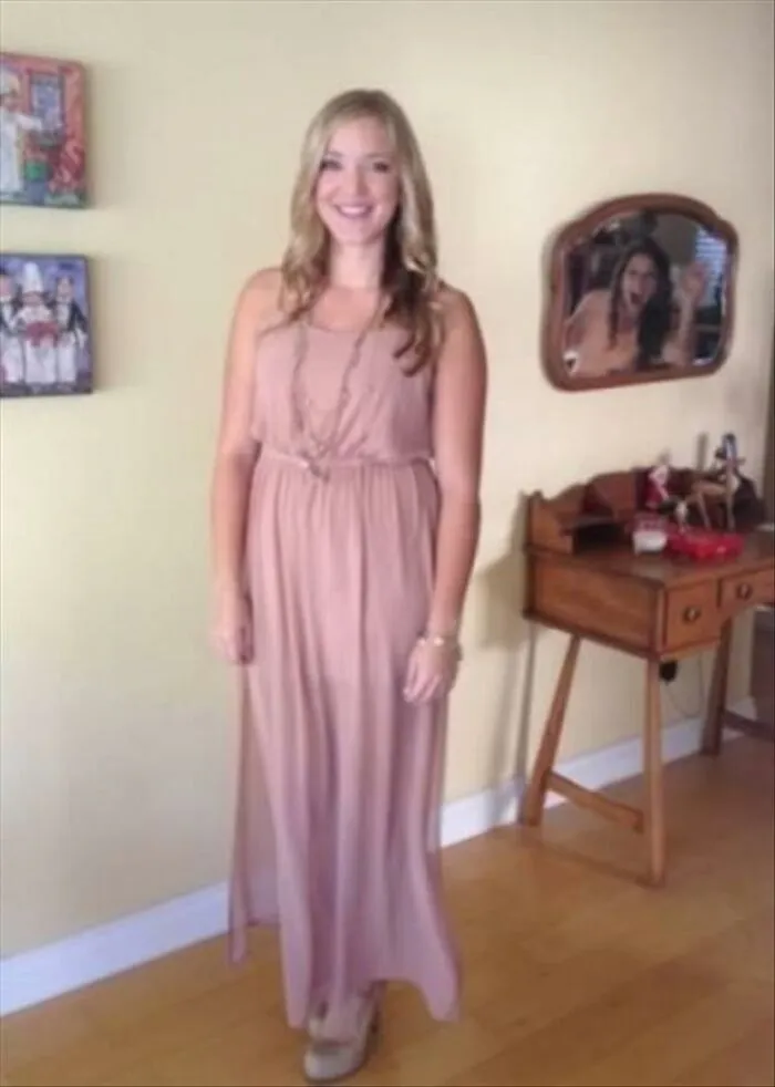 Humorous mirror pic showing a woman posing in a long pink dress with a funny expression caught in the background mirror.